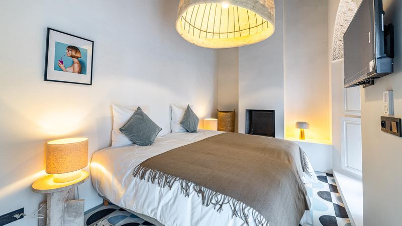 Bedroom 1: the beds under a brown throw, two lit lamps, a large pendant lamp and a picture on the wall.