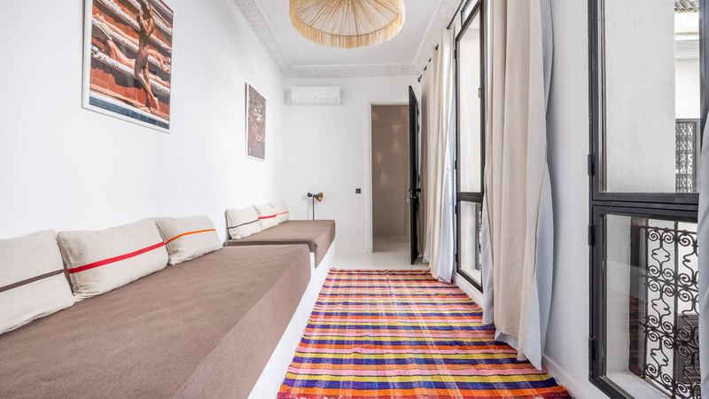 Bedroom 2: two single beds along the wall, a multicoloured striped rug and wrought-iron windows with pale curtains.