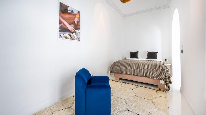 Bedroom 2: the queen bed under a houndstooth throw, a blue velvet armchair and a photograph on the wall.