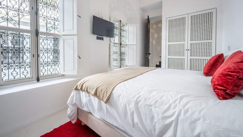 Bedroom 3: the queen bed with red velvet cushions, a red rug and wrought-iron windows with white shutters.
