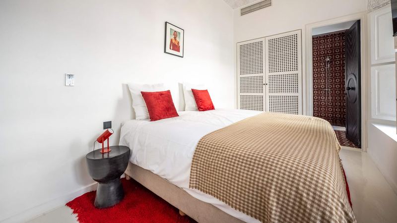 Bedroom 3: the queen bed under a checked throw, a red lamp on a black bedside table and an open black door.