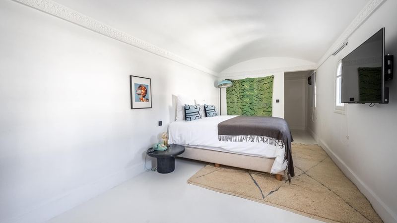 Bedroom 4: the queen bed under a grey throw, a pale rug, a green hanging on the wall and a vaulted ceiling.