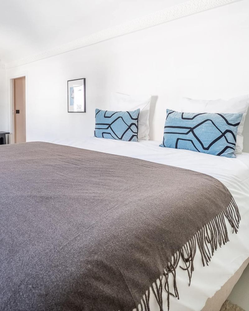La chambre 4 : le lit queen et ses coussins bleus à motifs, contre un mur blanc.