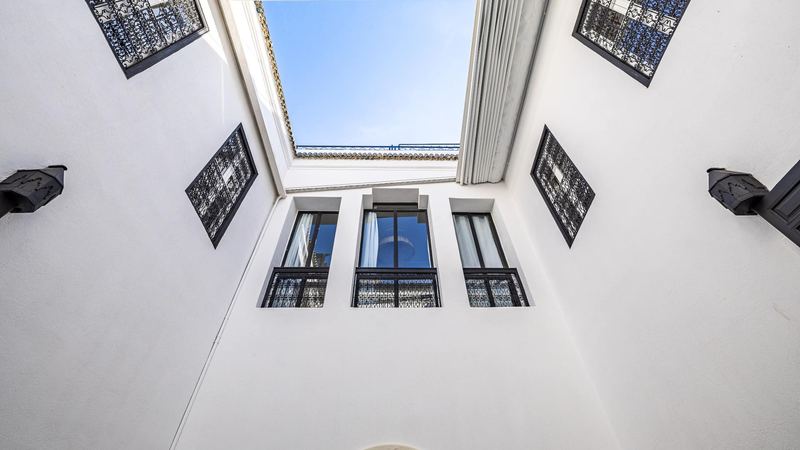 The sky above the courtyard, seen from below, between white walls and wrought-iron windows.