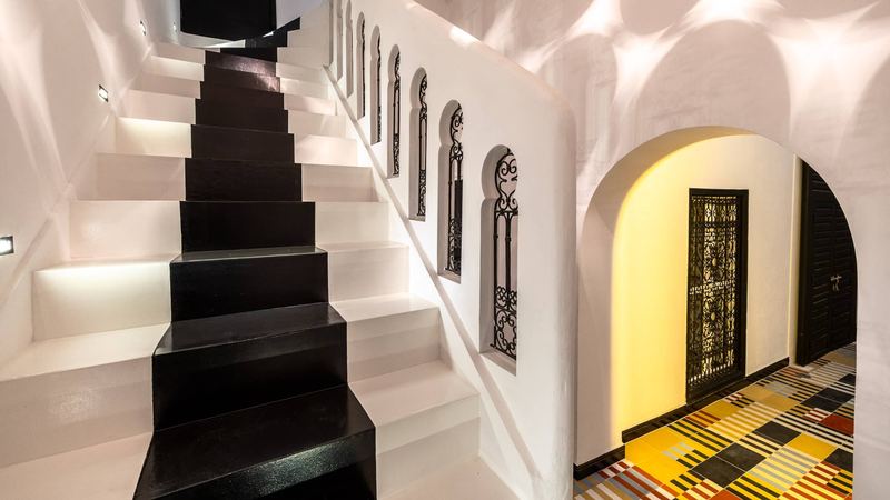 The white stairs with their black runner and small wrought-iron windows; under an arch, a wrought-iron door and a yellow and black cement-tile floor.