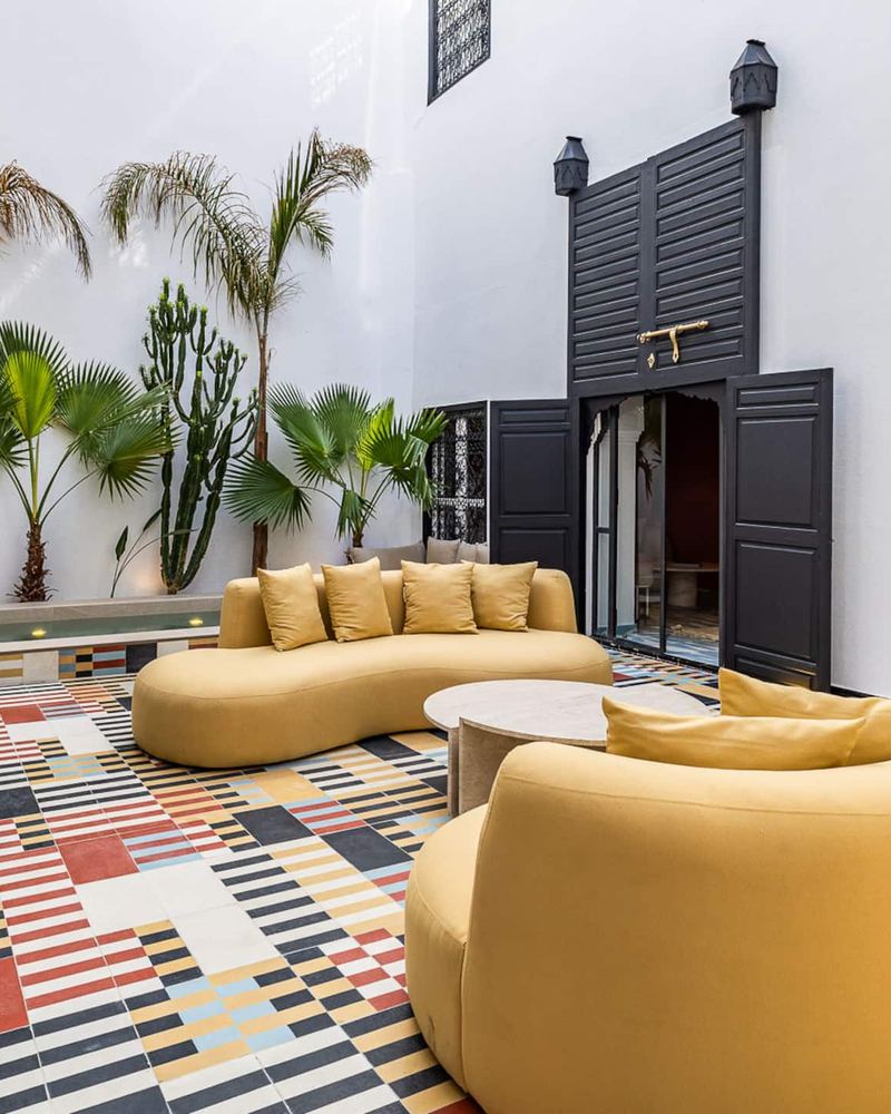 Les deux canapés courbes couleur moutarde autour d’une table basse ronde, avec la piscine et les palmiers au fond.