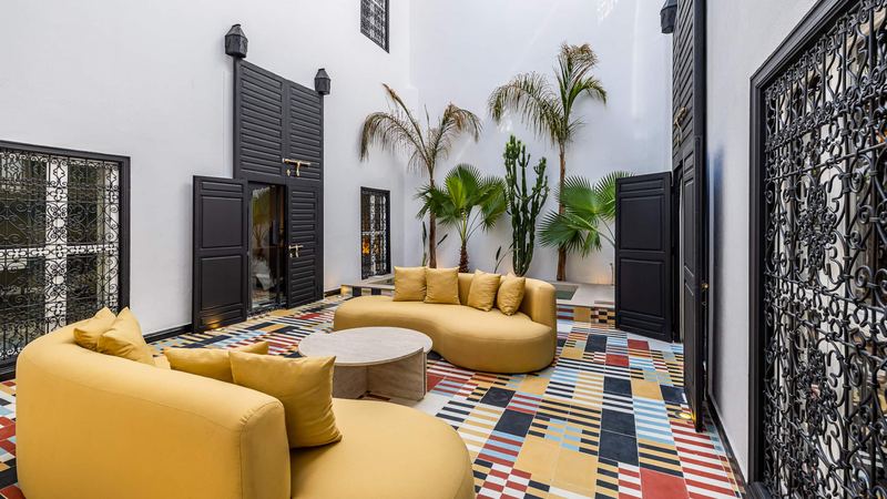 The courtyard: two curved mustard sofas around a round low table, the tall black doors and, in front, a wrought-iron screen.