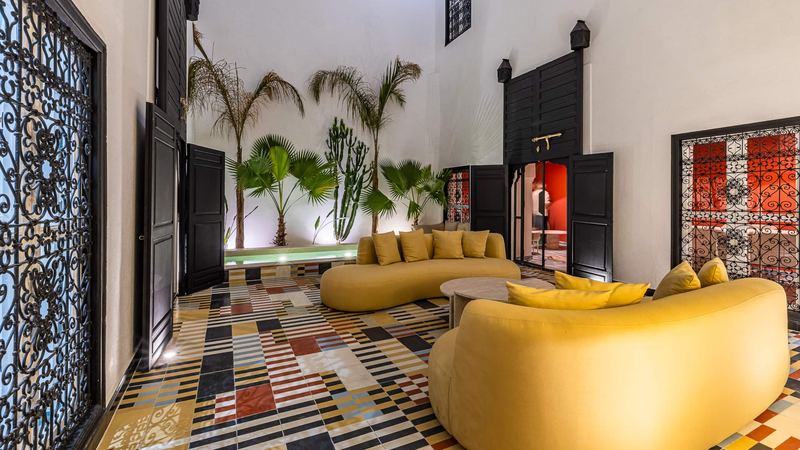 The courtyard: the mustard sofas, palms against the white wall, the black doors open onto the pink sitting room and, in front, a wrought-iron screen.