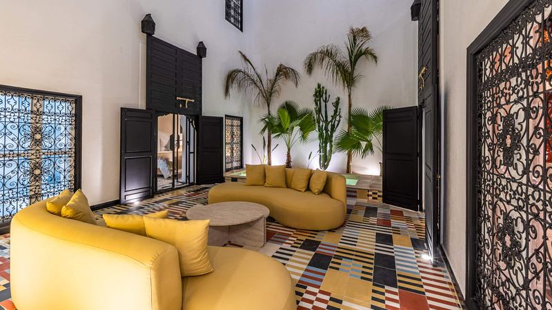 The courtyard between two wrought-iron screens: the curved mustard sofas, the round low table and the palms.