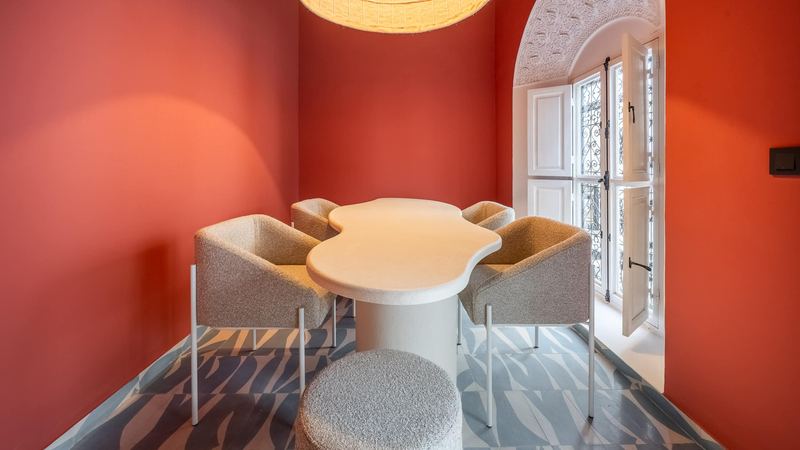 The dining area: a rounded white table, bouclé chairs and a wrought-iron window, against terracotta-pink walls.