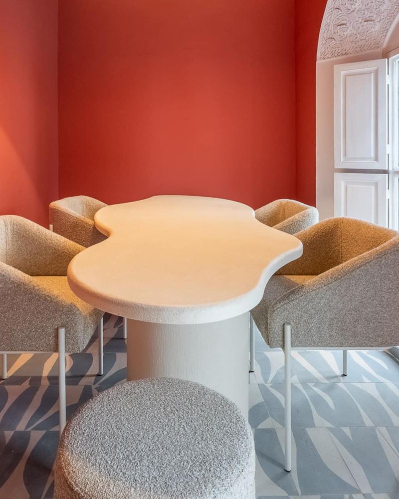 L’espace repas : une table blanche arrondie, des chaises en bouclette et une fenêtre en fer forgé, contre les murs rose terracotta.