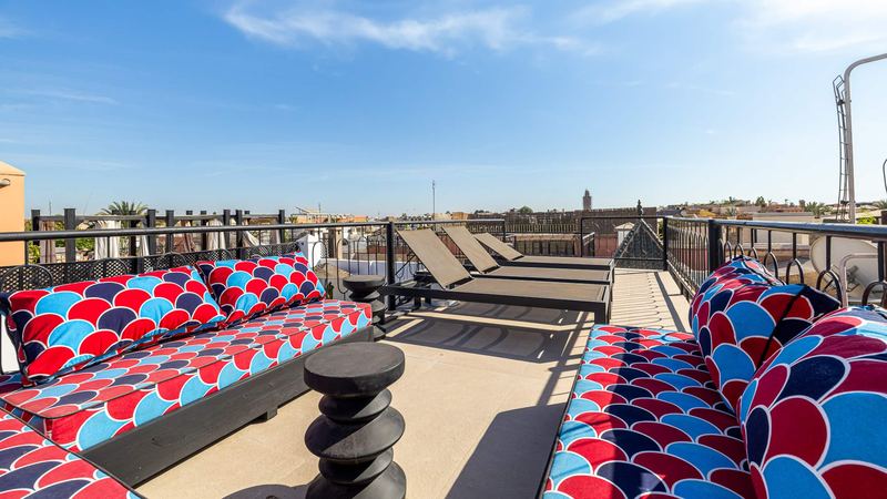 The roof terrace: sofas with red and blue cushions, sun loungers and, beyond, the rooftops of the medina under a blue sky.