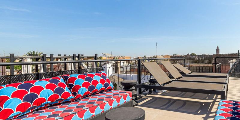 Le rooftop : banquettes aux coussins rouges et bleus, transats et, au loin, les toits de la médina sous un ciel bleu.