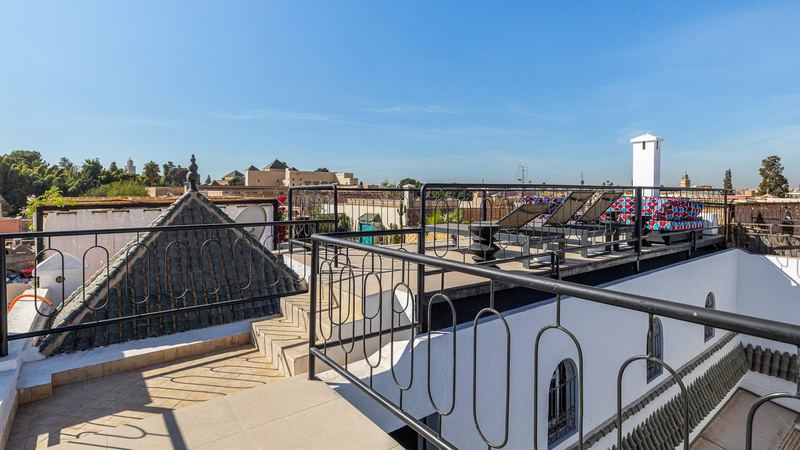 From the roof terrace: a pointed green-tiled roof behind the black iron railing and, beyond, palm trees and the rooftops of the medina.