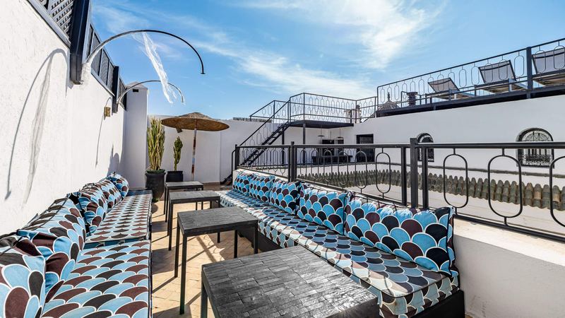 A terrace with long sofas, blue and brown cushions, black low tables and a stair to the upper terrace.