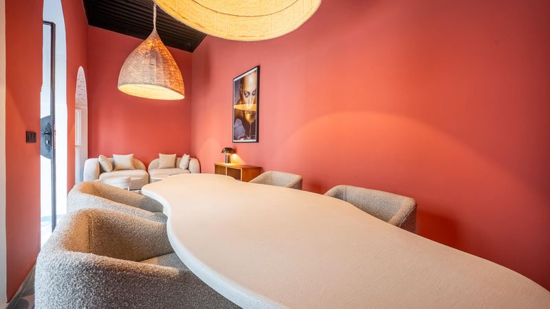 The terracotta-pink sitting room: the long rounded white table, bouclé armchairs and woven pendant lamps.