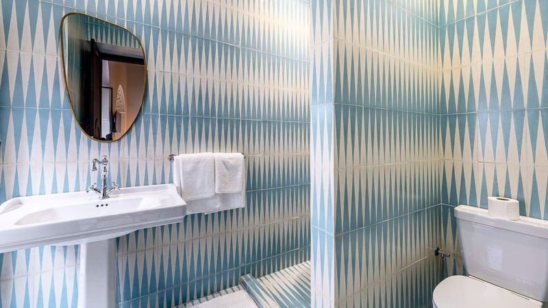 A bathroom with blue and white tiles, a pedestal basin and a mirror.