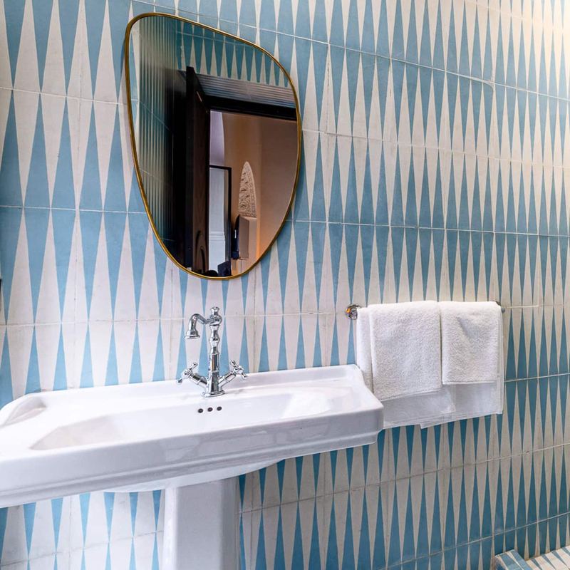Une salle de bain aux carreaux bleus et blancs, avec un lavabo sur colonne et un miroir.