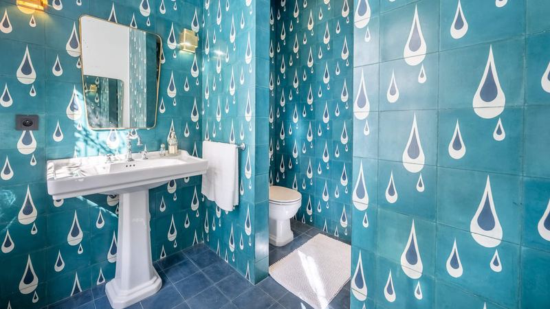 A bathroom tiled in teal with a drop pattern, a pedestal basin and a mirror.