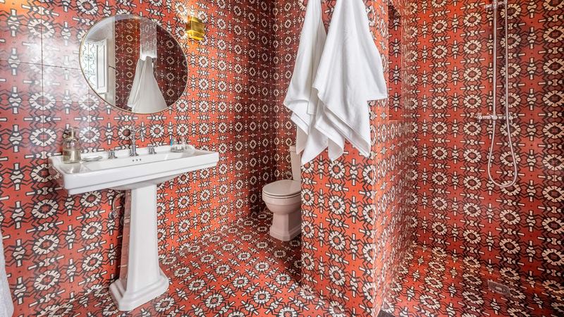 A bathroom with patterned red tiles, a pedestal basin and a round mirror.
