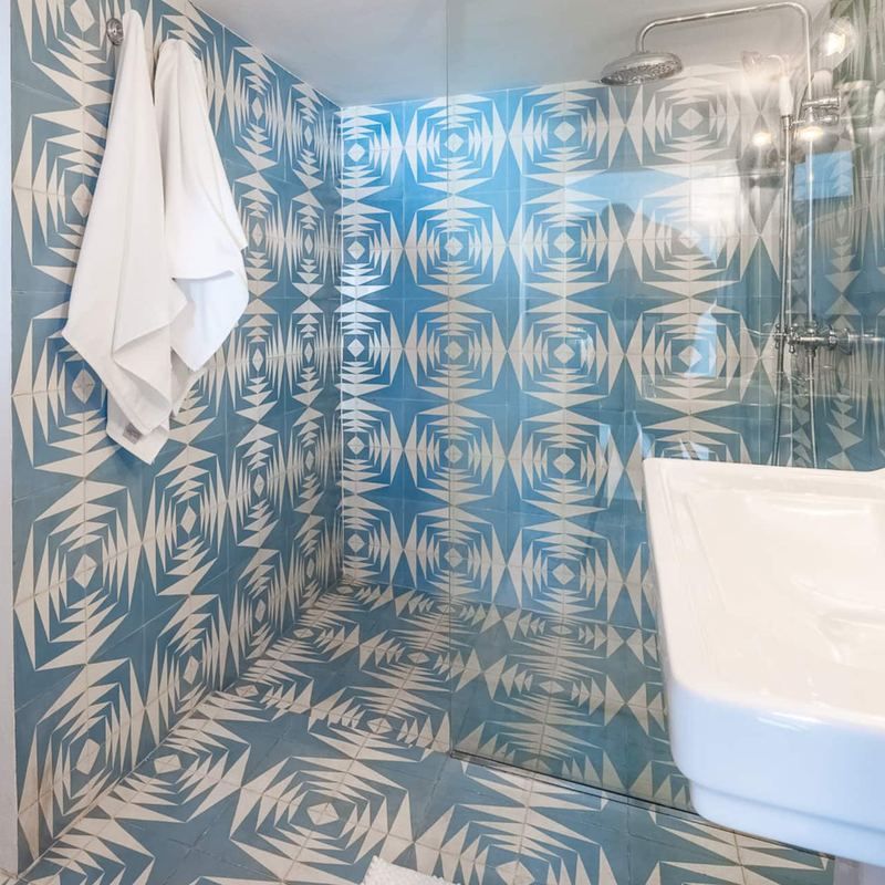 Une salle de bain aux carreaux bleus à motifs géométriques, avec une serviette suspendue et un lavabo.